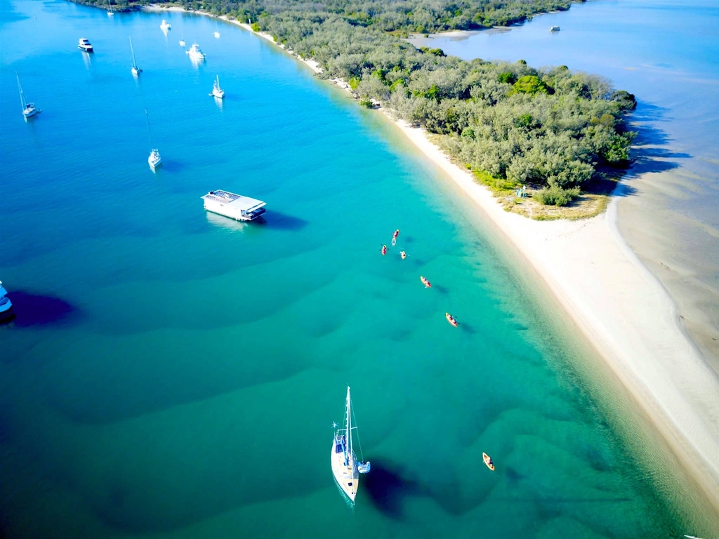 Aerial view of turquoise Gold Coast waters, sandspit beach and forested island with boats and kayaks